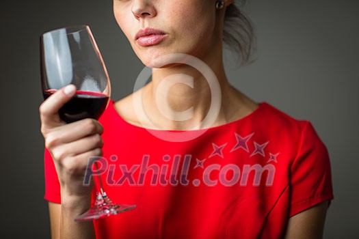 Elegant young woman in a red dress, having a glass of red wine