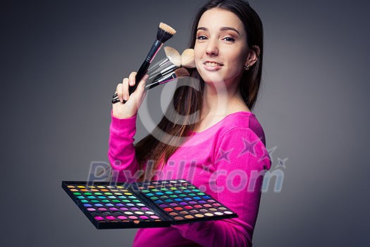 Cute make-up artist holding her vast palette of colors and hands with brushes around her (color toned image) Cute make-up artist holding her vast palette of colors and hands with brushes around her (color toned image)