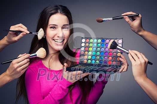 Cute make-up artist holding her vast palette of colors and hands with brushes around her (color toned image) Cute make-up artist holding her vast palette of colors and hands with brushes around her (color toned image)