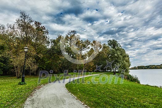 Path in autumn park near the lake with dramatic sky Path in autumn park near the lake with dramatic sky