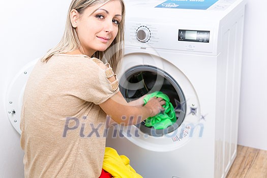 Housework: young woman doing laundry - putting colorful garments into the washing machine (shallow DOF; color toned image) Housework: young woman doing laundry - putting colorful garments into the washing machine (shallow DOF; color toned image)