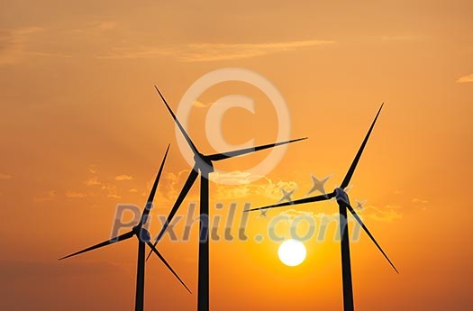 Green renewable energy concept - wind generator turbines in sky on sunset Green renewable energy concept - wind generator turbines in sky on sunset