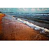 Vintage retro hipster style travel image of wave surging on sand on beach with grunge texture overlaid