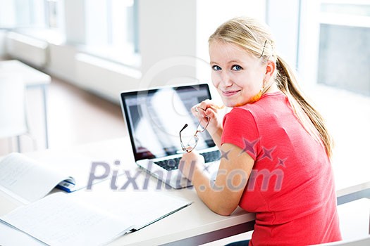 In the library - pretty, female student with books, papers and laptop computer working in a high school library (color toned image) In the library - pretty, female student with books, papers and laptop computer working in a high school library (color toned image)