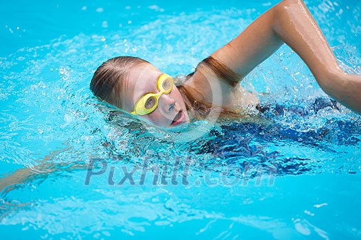 Young girl in goggles and cap swimming crawl stroke style in the blue water pool Young girl in goggles and cap swimming crawl stroke style in the blue water pool