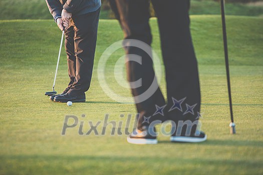 Golf green sceen - golfer putting near the hole, short putt (colort toned image with reduced contrast and some added noise) Golf green sceen - golfer putting near the hole, short putt (colort toned image with reduced contrast and some added noise)