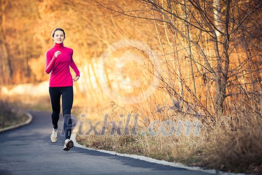 Young woman running outdoors in a city park on a cold fall/winter day Young woman running outdoors in a city park on a cold fall/winter day