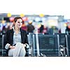 Young female passenger at the airport, using her tablet computer while waiting for her flight (color toned image)