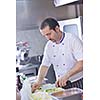 Handsome chef dressed in white uniform decorating pasta salad and seafood fish in modern kitchen