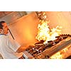 Handsome chef dressed in white uniform decorating pasta salad and seafood fish in modern kitchen