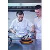 Handsome chef dressed in white uniform decorating pasta salad and seafood fish in modern kitchen