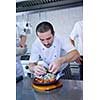 Handsome chef dressed in white uniform decorating pasta salad and seafood fish in modern kitchen