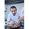 Handsome chef dressed in white uniform decorating pasta salad and seafood fish in modern kitchen