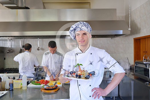 Handsome chef dressed in white uniform decorating pasta salad and seafood fish in modern kitchen Handsome chef dressed in white uniform decorating pasta salad and seafood fish in modern kitchen