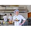 Handsome chef dressed in white uniform decorating pasta salad and seafood fish in modern kitchen