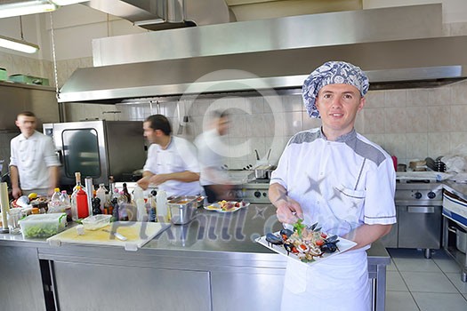 Handsome chef dressed in white uniform decorating pasta salad and seafood fish in modern kitchen