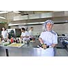 Handsome chef dressed in white uniform decorating pasta salad and seafood fish in modern kitchen