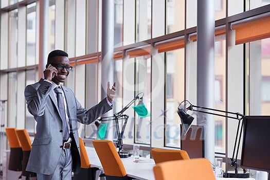 Happy smiling successful African American businessman in a suit in a modern bright office indoors speel on phone Happy smiling successful African American businessman in a suit in a modern bright office indoors speel on phone