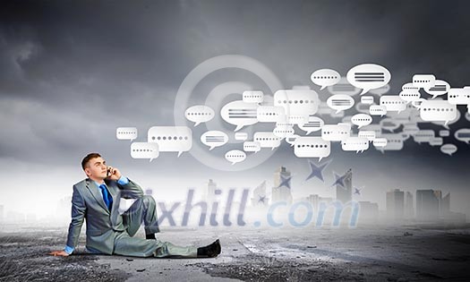 Image of young businessman with mobile phone sitting on floor Image of young businessman with mobile phone sitting on floor