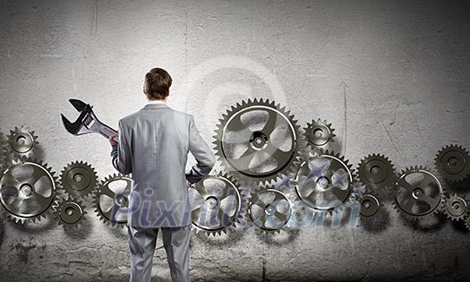 Young businessman with wrench against mechanism background Young businessman with wrench against mechanism background