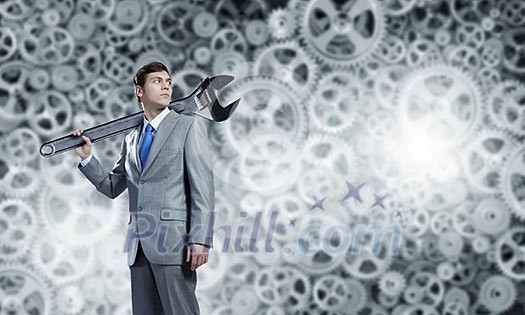 Young businessman with wrench against mechanism background Young businessman with wrench against mechanism background