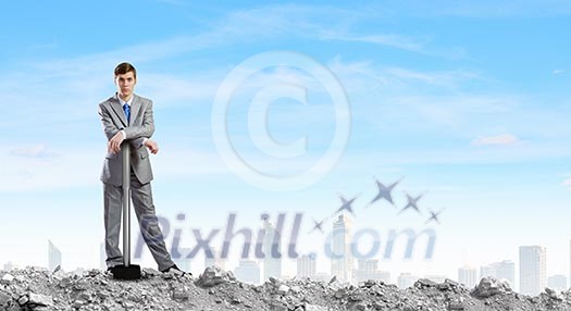 Young businessman with hammer standing on ruins Young businessman with hammer standing on ruins