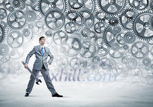 Young businessman with wrench against mechanism background Young businessman with wrench against mechanism background
