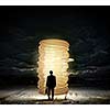 Rear view of businessman with suitcase looking at stack of coins