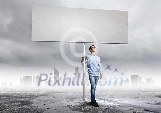 Young man against city background holding blank banner. Place for text Young man against city background holding blank banner. Place for text