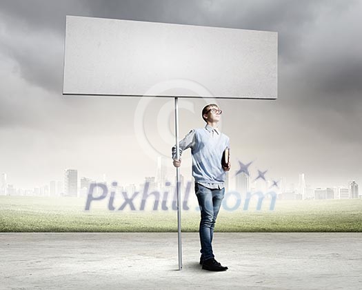Young man against city background holding blank banner. Place for text Young man against city background holding blank banner. Place for text