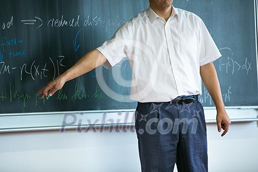teacher teaching mathematics while pointing at blackboard in classroom teacher teaching mathematics while pointing at blackboard in classroom