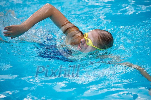 Young girl in goggles and cap swimming crawl stroke style in the blue water pool Young girl in goggles and cap swimming crawl stroke style in the blue water pool