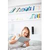 Pretty, young woman lying in bed, using her tablet computer, reading sending e-mails, using apps, having fun