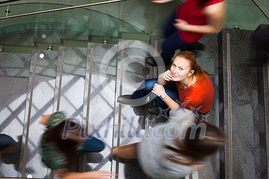 At the university/college - Students rushing up and down a busy stairway - confident pretty young female student looking upwards (color toned image) At the university/college - Students rushing up and down a busy stairway - confident pretty young female student looking upwards (color toned image)