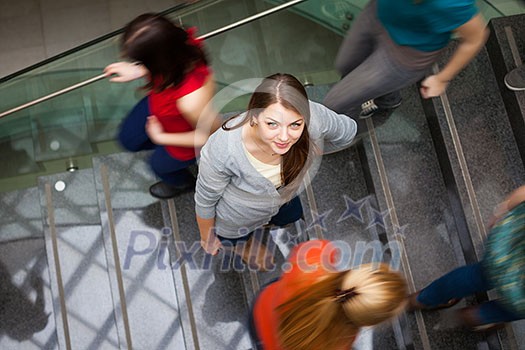 At the university/college - Students rushing up and down a busy stairway - confident pretty young female student looking upwards (color toned image) At the university/college - Students rushing up and down a busy stairway - confident pretty young female student looking upwards (color toned image)