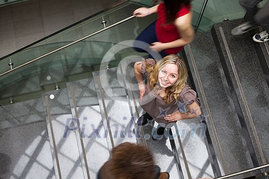 At the university/college - Students rushing up and down a busy stairway - confident pretty young female student looking upwards (color toned image) At the university/college - Students rushing up and down a busy stairway - confident pretty young female student looking upwards (color toned image)