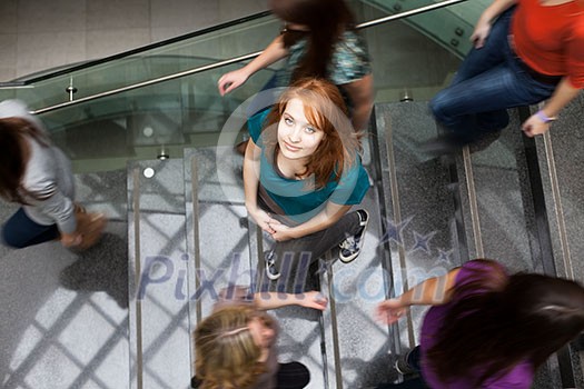 At the university/college - Students rushing up and down a busy stairway - confident pretty young female student looking upwards (color toned image) At the university/college - Students rushing up and down a busy stairway - confident pretty young female student looking upwards (color toned image)