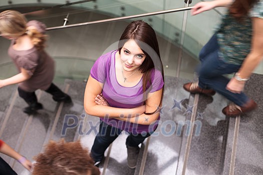 At the university/college - Students rushing up and down a busy stairway - confident pretty young female student looking upwards (color toned image) At the university/college - Students rushing up and down a busy stairway - confident pretty young female student looking upwards (color toned image)