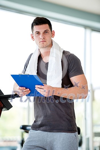 Portrait of a smiling male trainer with clipboard standing in a bright gym Portrait of a smiling male trainer with clipboard standing in a bright gym