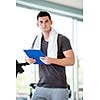 Portrait of a smiling male trainer with clipboard standing in a bright gym