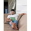 Handsome relaxed young businessman working from home on tablet computer