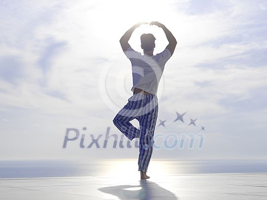 handsome young man practicing yoga on in modern home terace with ocean and sunset in background handsome young man practicing yoga on in modern home terace with ocean and sunset in background