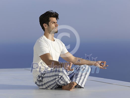 handsome young man practicing yoga on in modern home terace with ocean and sunset in background handsome young man practicing yoga on in modern home terace with ocean and sunset in background