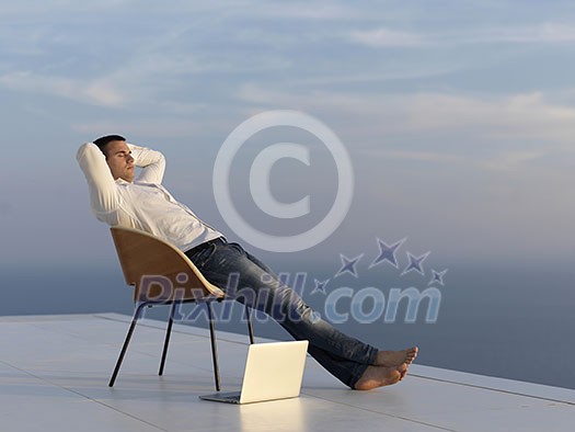 handsome young man relaxing and working on laptop computer at home balcony while looking sunset handsome young man relaxing and working on laptop computer at home balcony while looking sunset