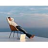 handsome young man relaxing and working on laptop computer at home balcony while looking sunset