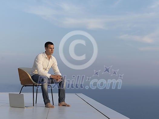 handsome young man relaxing and working on laptop computer at home balcony while looking sunset handsome young man relaxing and working on laptop computer at home balcony while looking sunset