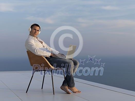 handsome young man relaxing and working on laptop computer at home balcony while looking sunset handsome young man relaxing and working on laptop computer at home balcony while looking sunset