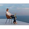 handsome young man relaxing and working on laptop computer at home balcony while looking sunset