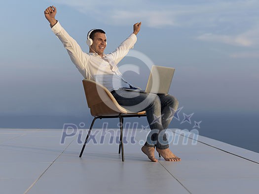 handsome young man relaxing and working on laptop computer at home balcony while looking sunset handsome young man relaxing and working on laptop computer at home balcony while looking sunset