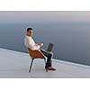 handsome young man relaxing and working on laptop computer at home balcony while looking sunset